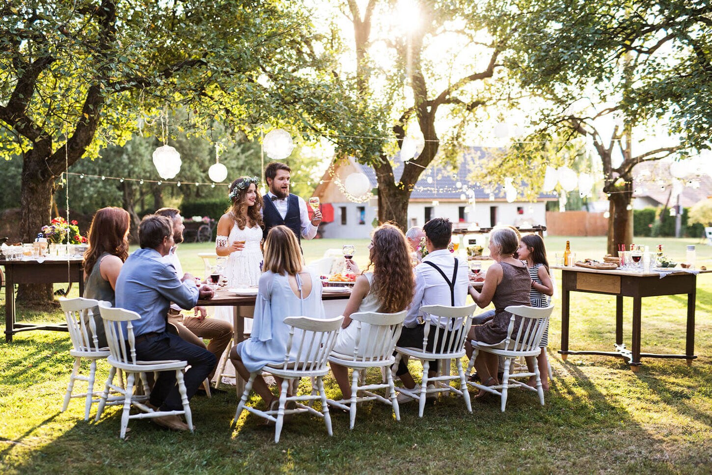 Backyard, micro-wedding with a couple and friends and family sitting at a table surrounded by trees