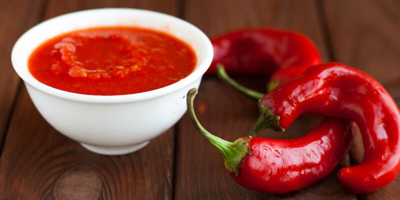 Cup of homemade hot sauce next to red chili peppers.