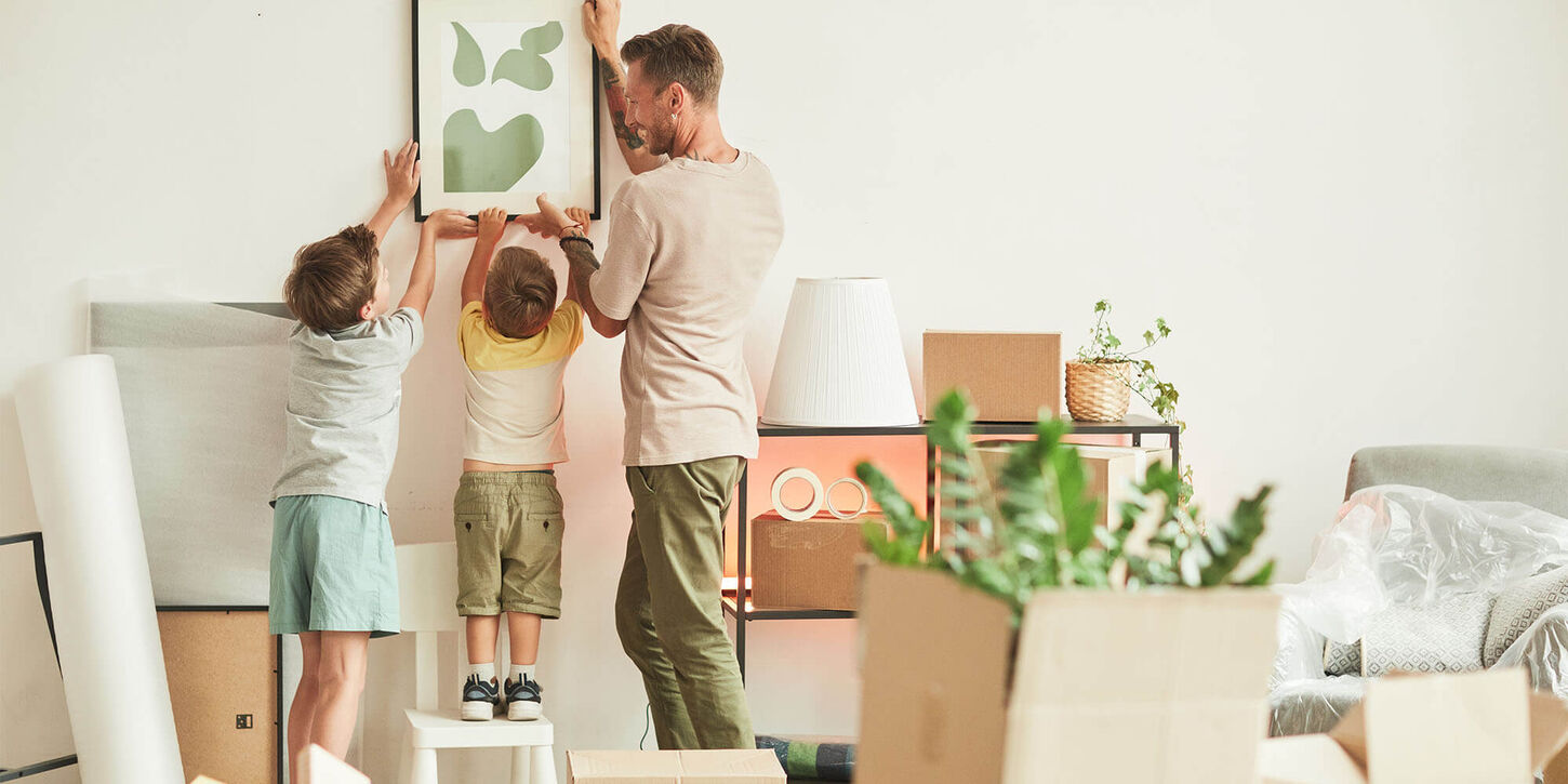 Man and his two sons unpacking their belongings from a move into a new house and hanging pictures on the wall