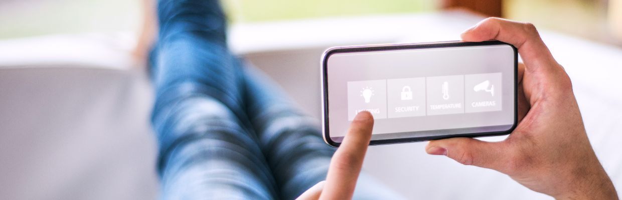 Person looking at smart home technology app on their mobile device while laying on sofa in living room