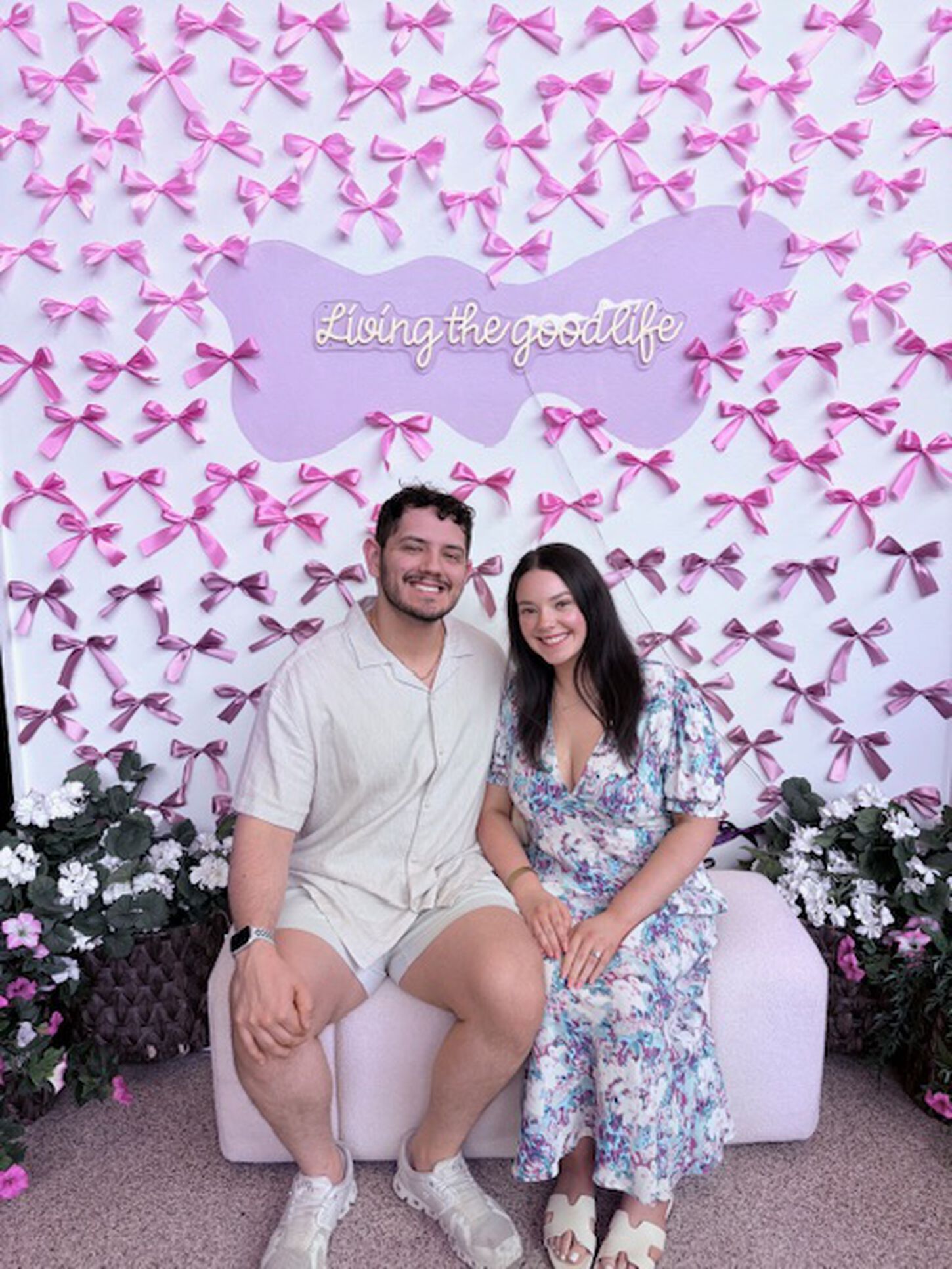 Ashley and Jonathan sitting in front of a photo op with a sign that reads living to good life