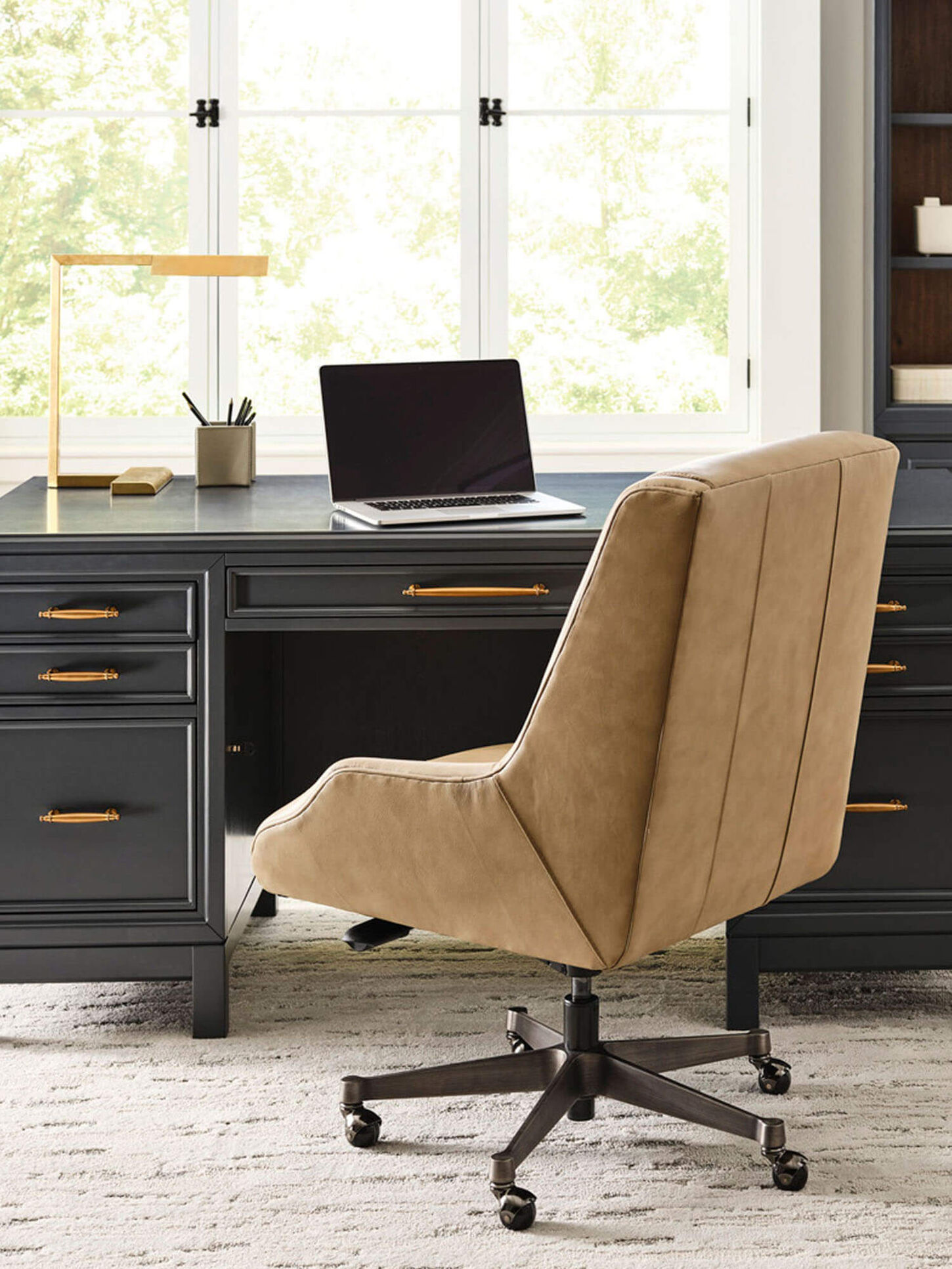 Dark desk in office with cozy brown chair and large windows.