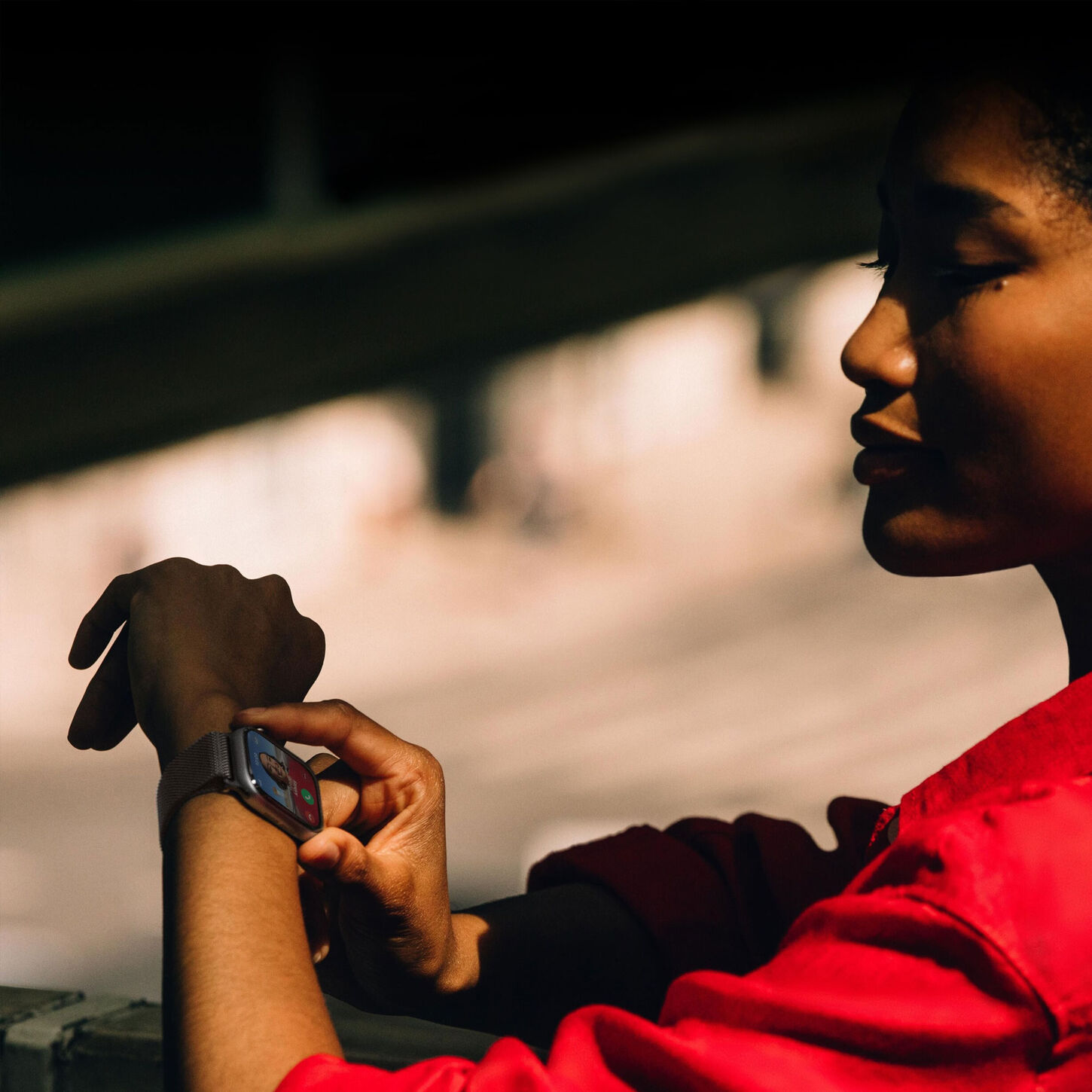 Close-up of a woman wearing a smartwatch and tapping the screen, with blurred background and warm lighting.