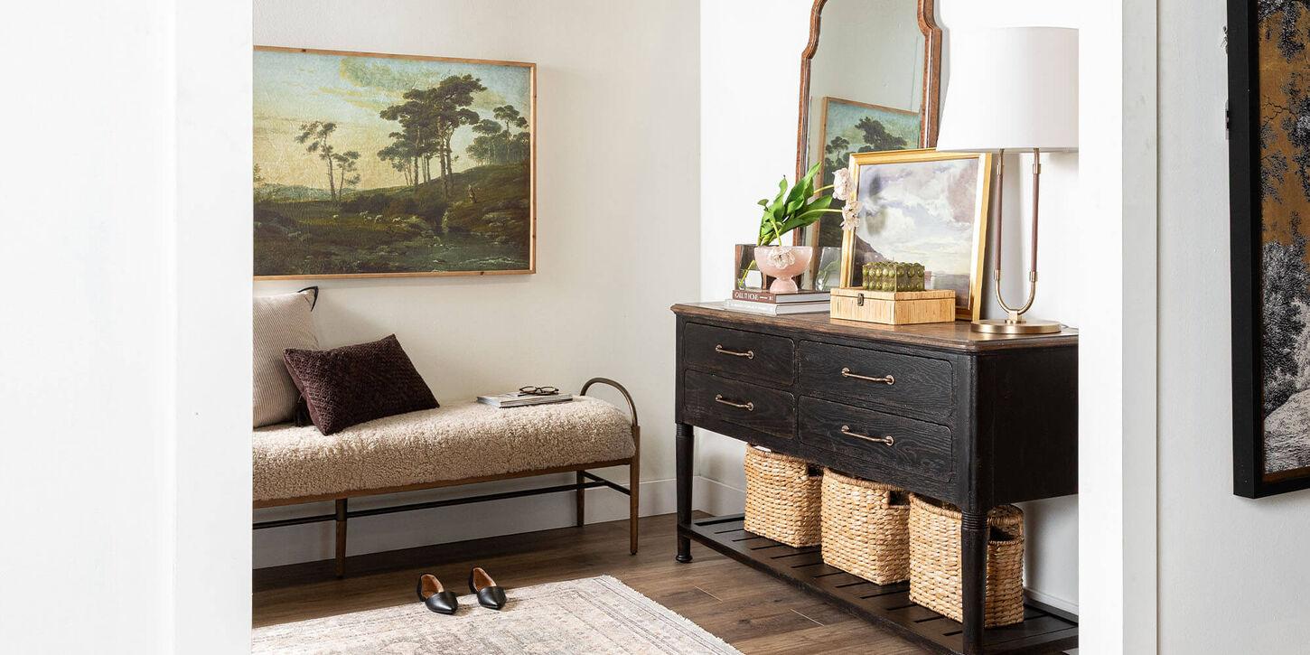 Entryway table and seat with lots of artwork, mirrors, a lamp and pillows