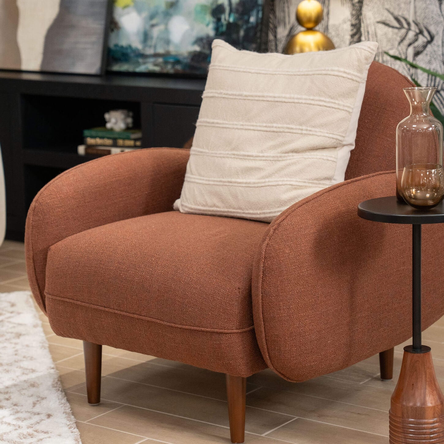 Brown chair with a white pillow next to a rug with a credenza in the background