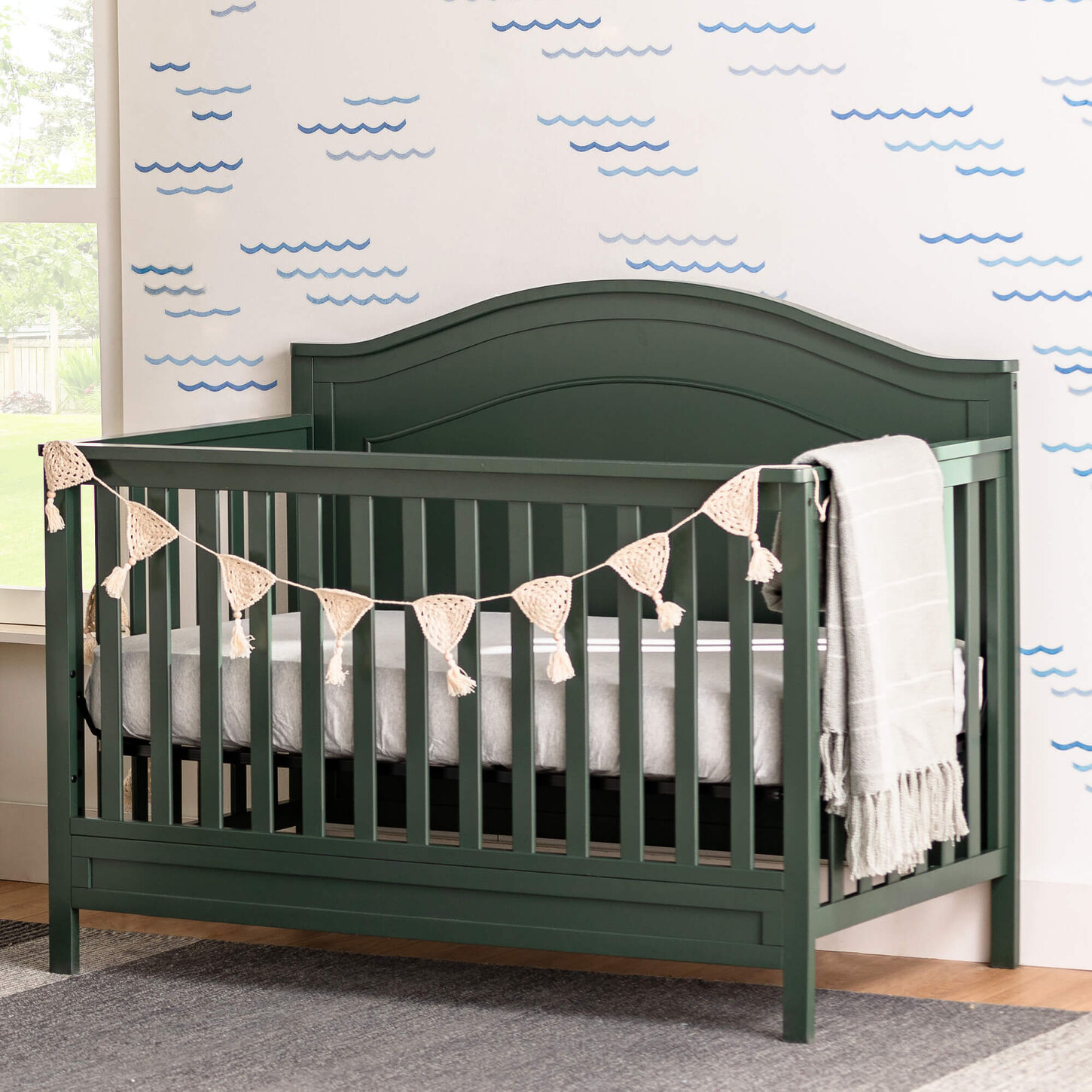 Green baby crib with blanket on side sitting in a bright nursery room