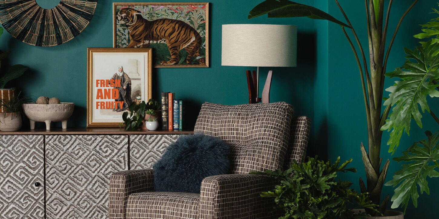 Blue wall with credenza filled with decor and art work, along with a chair, lamp and plants