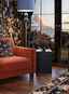A living room with burnt orange chair, blue tall lamp, rug, dark wallpaper and a big window.