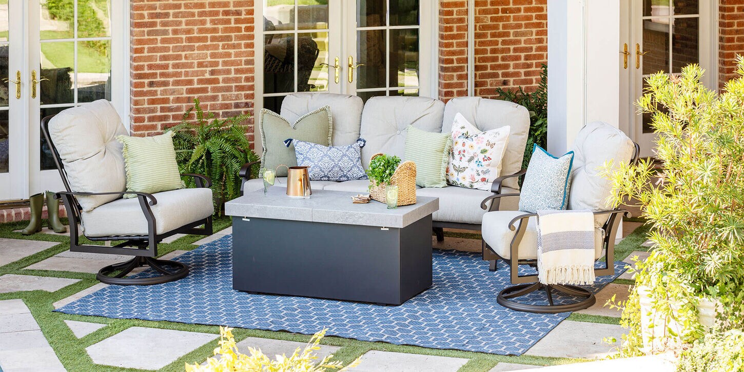 Outdoor patio furniture with a rug, sofa, chairs, fire pit, and plants