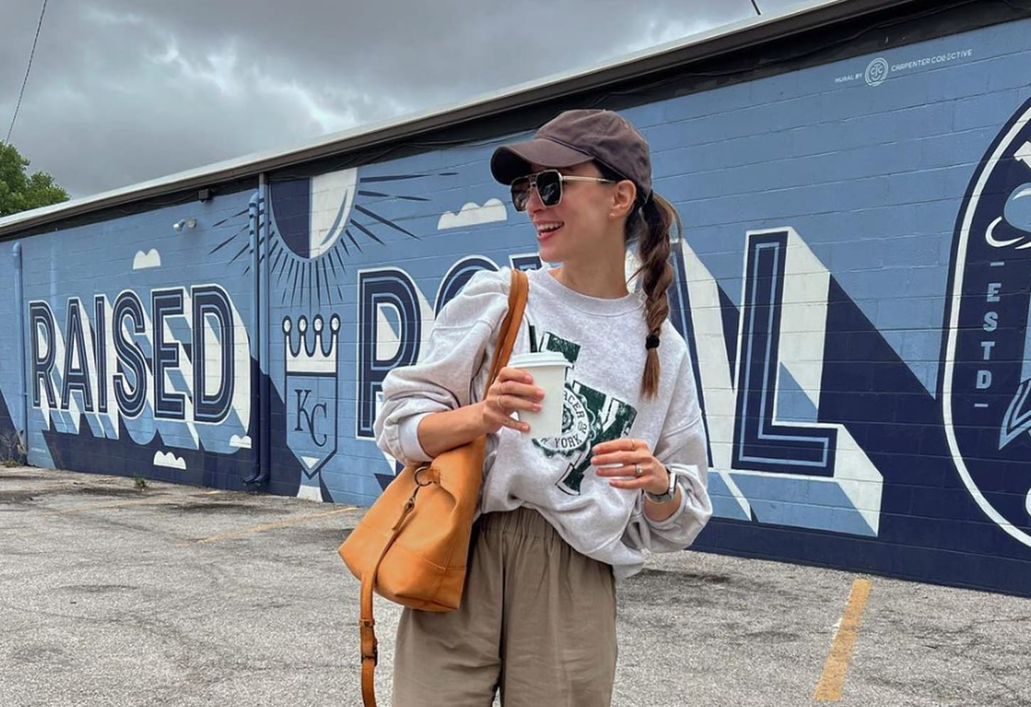 megan having a coffee outside standing in front of a mural