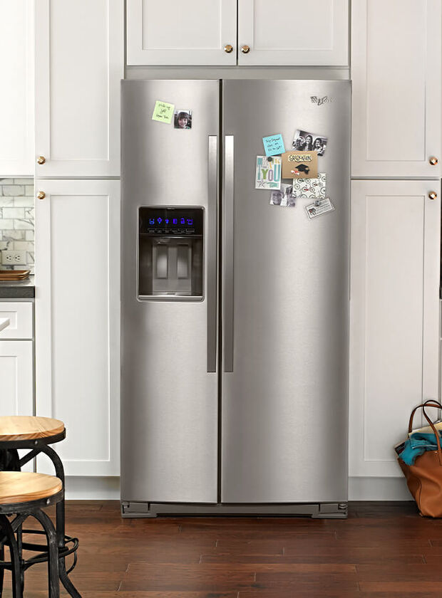 Whirlpool side by side refrigerator in home kitchen with magnets on front of fridge.