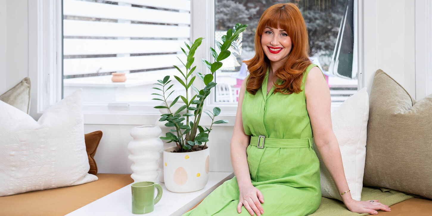 Sarah posing in her home next to a window, coffee cup, and plant
