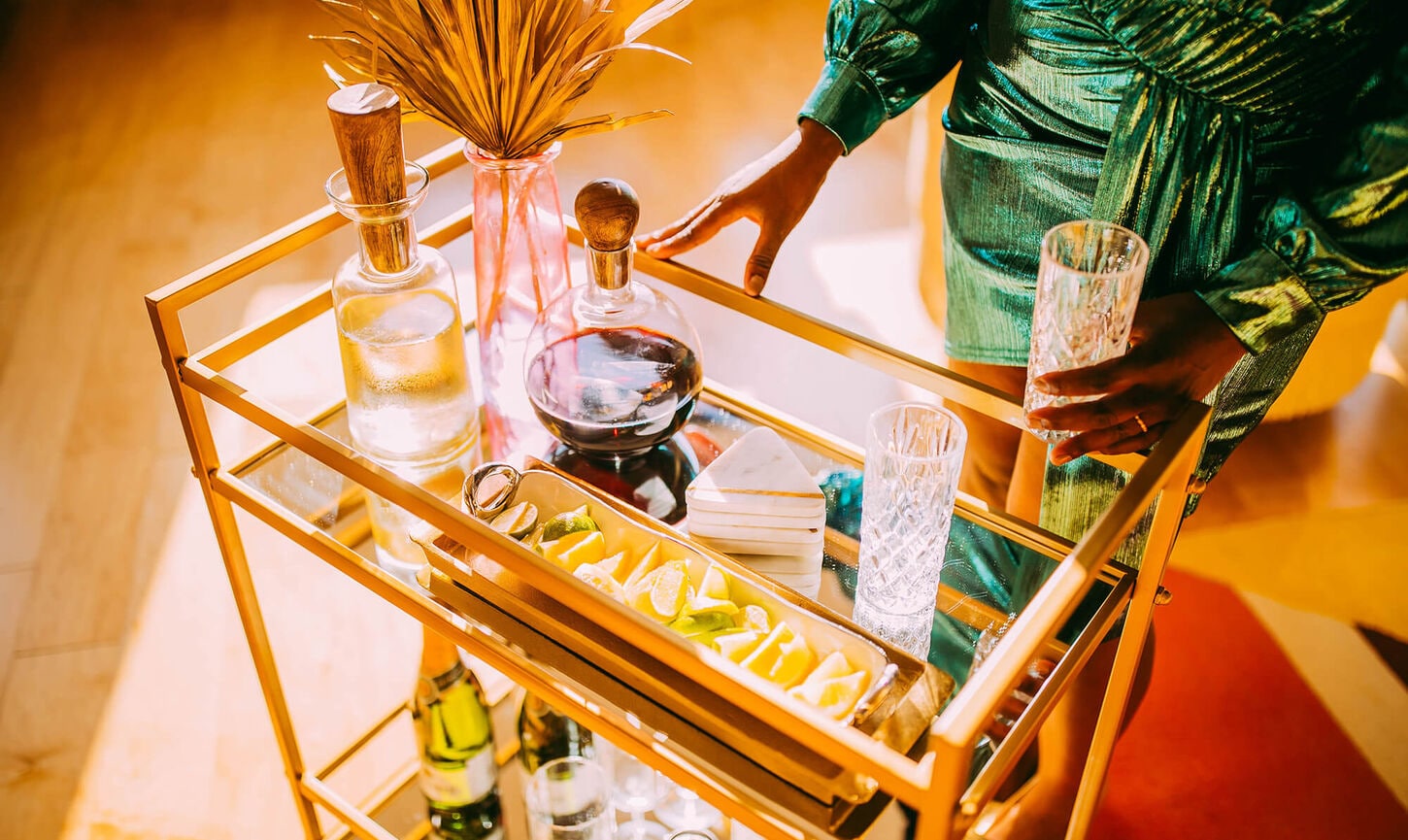 A woman grabbing for a drink on a gold bar cart
