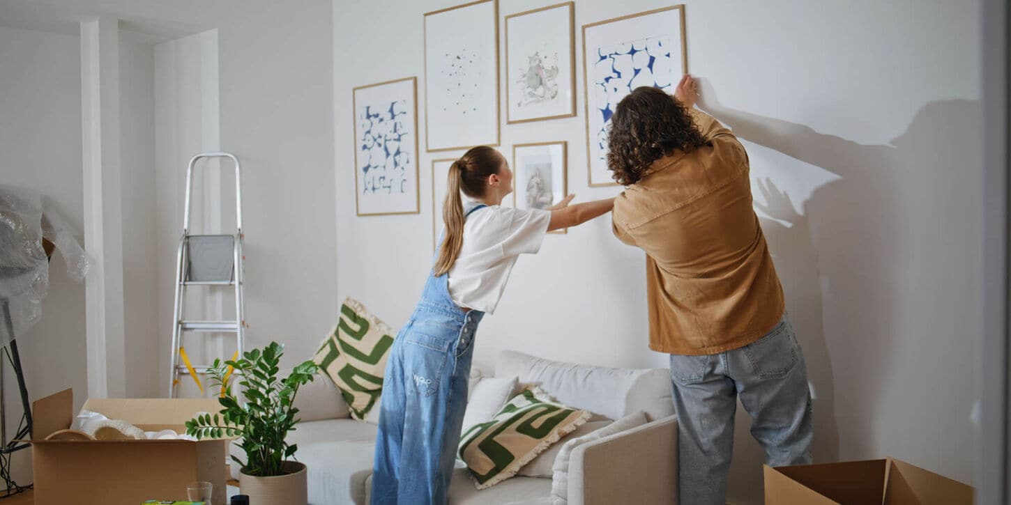 Couple hanging pictures on the wall in their new home with boxes around them