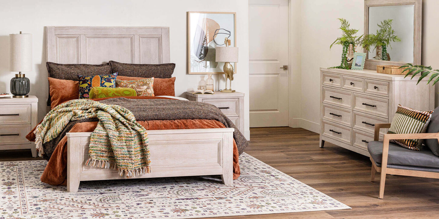 Bedroom with light wood bed and dresser, rust and brown bedding, patterned rug, and decorative accents.