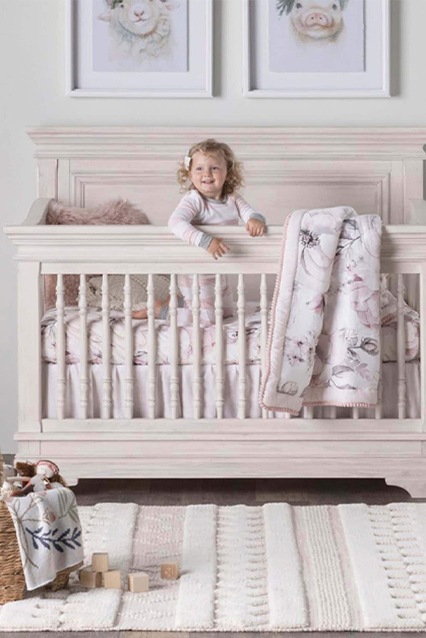 Baby in crib with rug, blanket and artwork on wall
