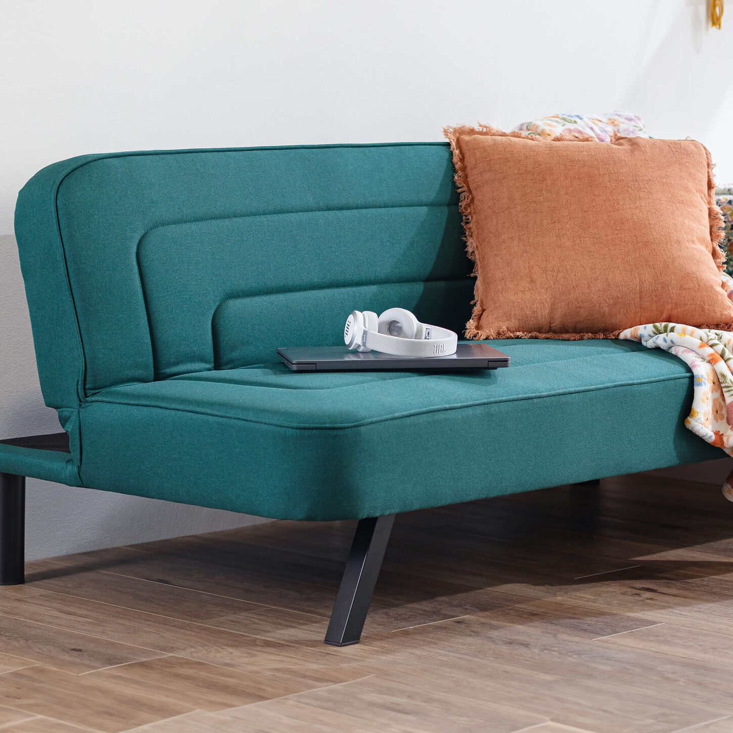 Green futon in a dorm room with an orange pillow