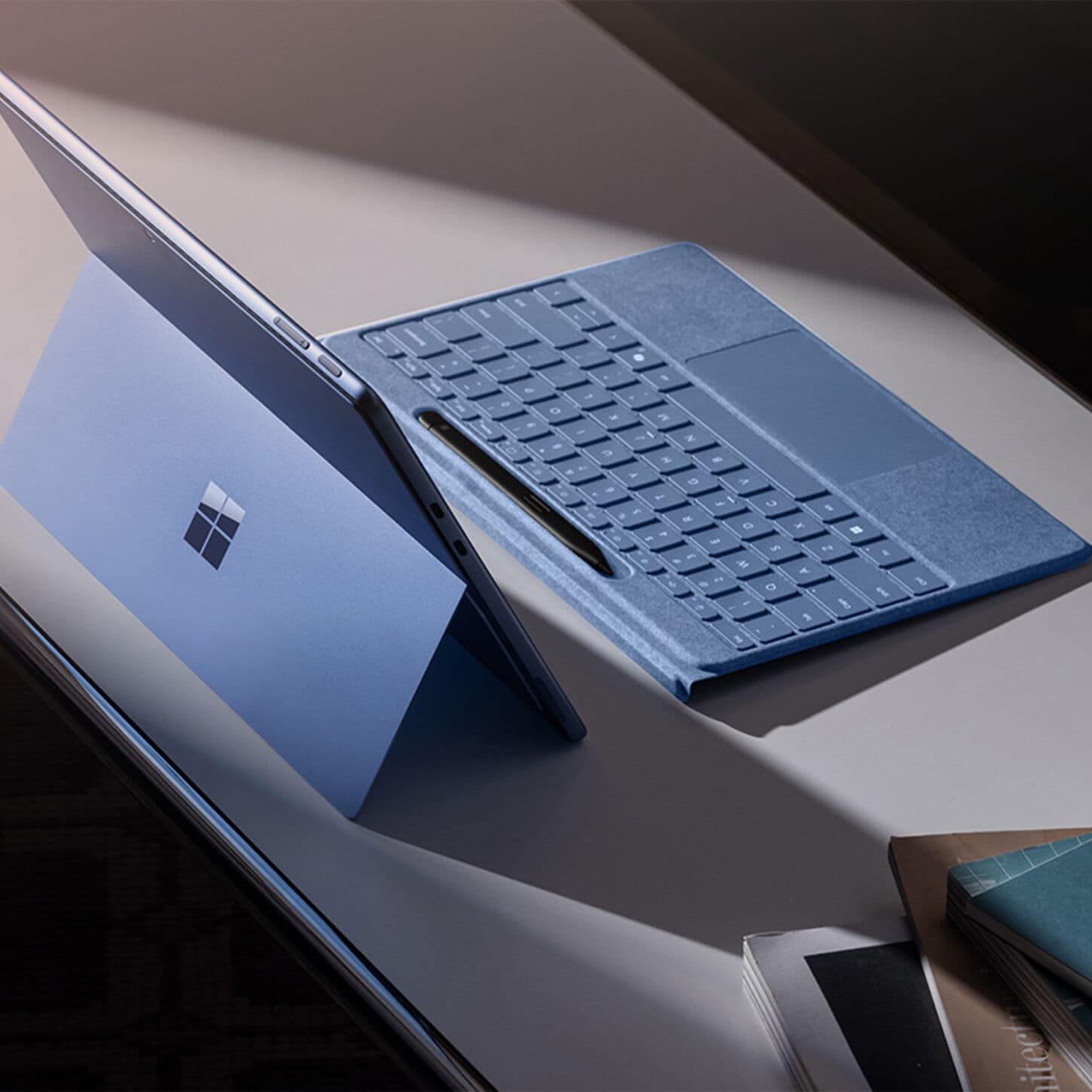 Blue surface copilot PC with keyboard and slim pen on desk.