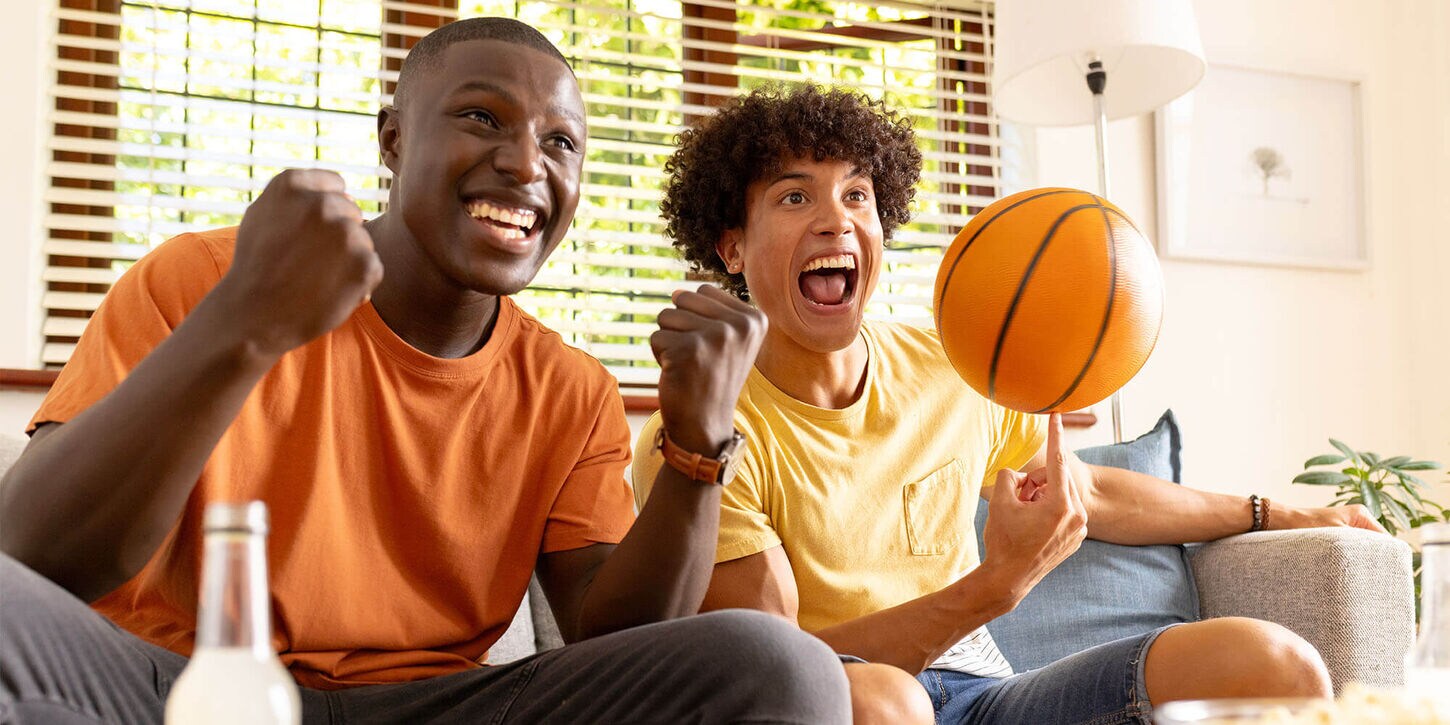 Two guys watching basketball and one holding a ball