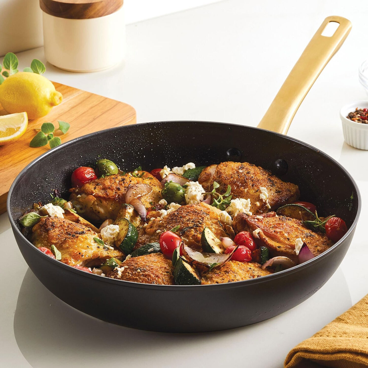Black skillet with gold handle and cooked chicken and vegetables.