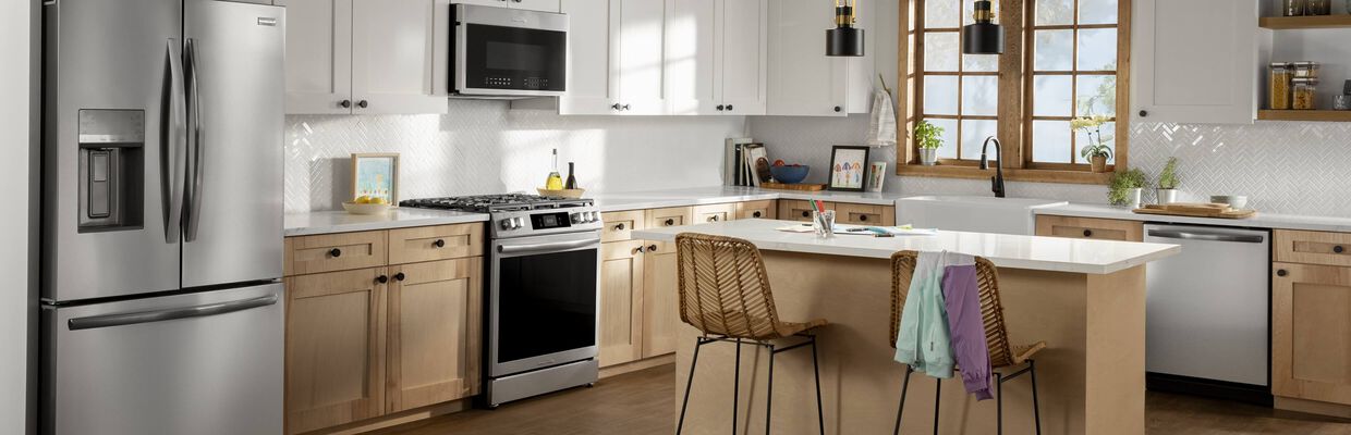 Modern kitchen with light wood cabinets, white countertops, and stainless steel appliances