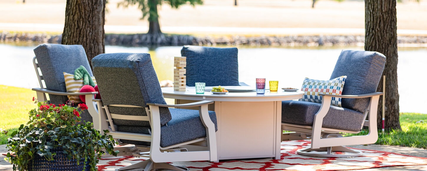 Outdoor patio setup with four cushioned chairs around a table holding drinks, snacks, and a block‑stacking game beside a lake.