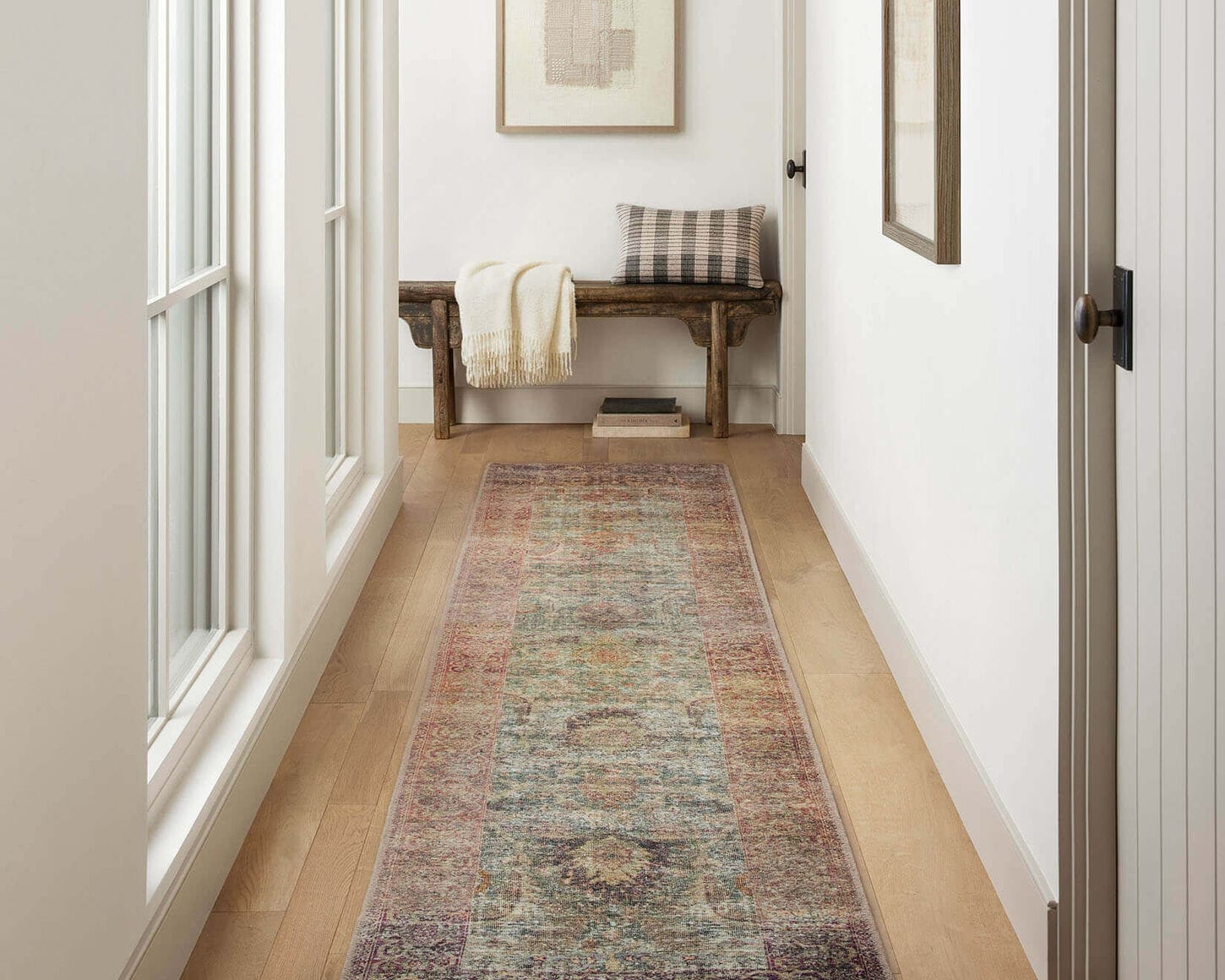 Hallway with runner rug and bench at the end of the hallway with a pillow, blanket and picture on the wall