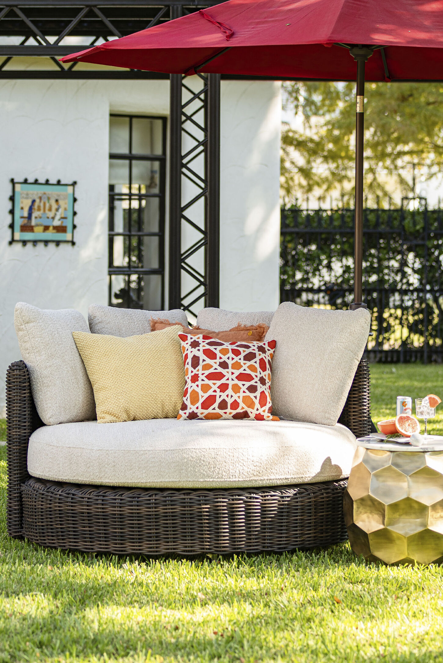 Outdoor furniture featuring a big round chair, pillows, and red umbrella in a backyard