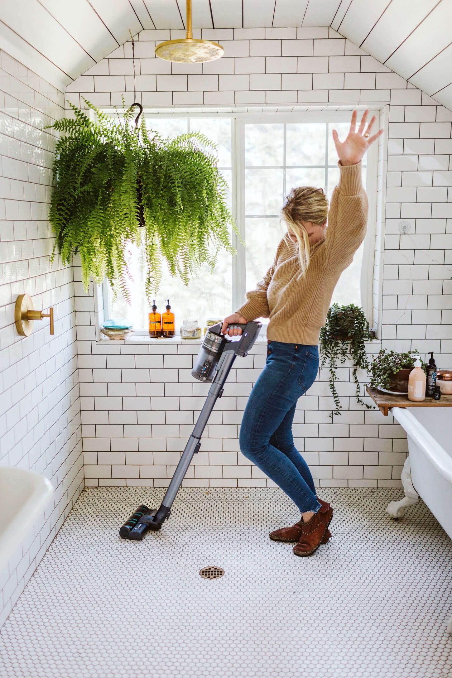 A woman cleaning her bathroom tile with a steam mop/vacuum while she is dancing