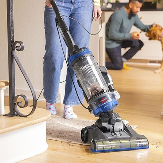 upright vacuum cleaning a runner rug on a light wood floor with man and dog in background